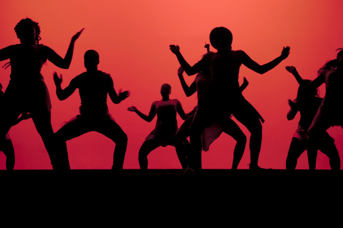 A dance showcase where students appear as silhouettes against an orange backdrop