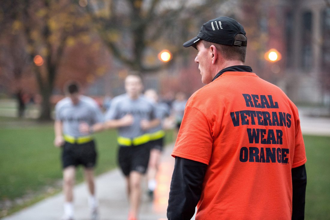 ROTC students running on the quad behind a man wearing a t-shirt that reads: 'real veterans wear orange'