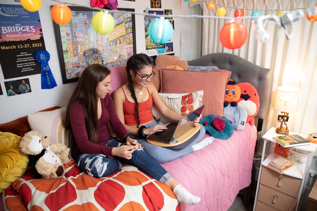 Two student sitting on bed and working in dorm room.