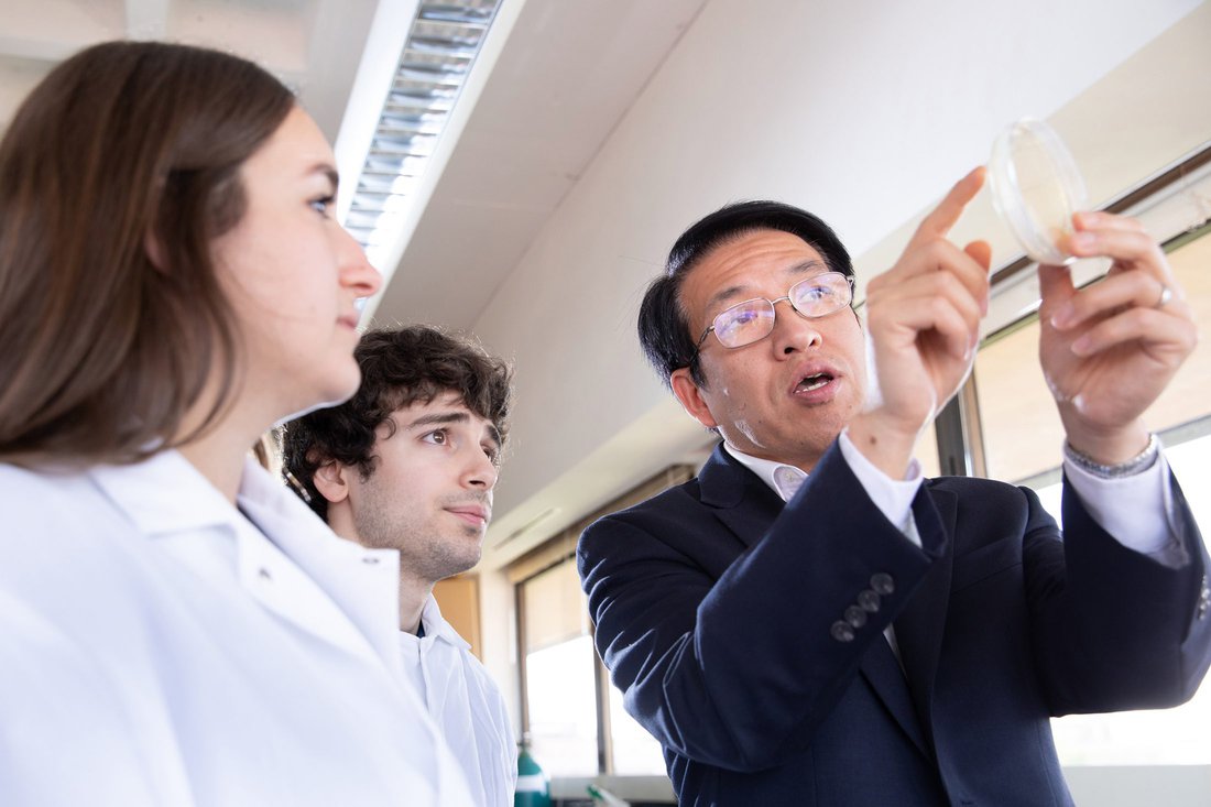 Professor points out an object in a pitri dish to students in lab coats.