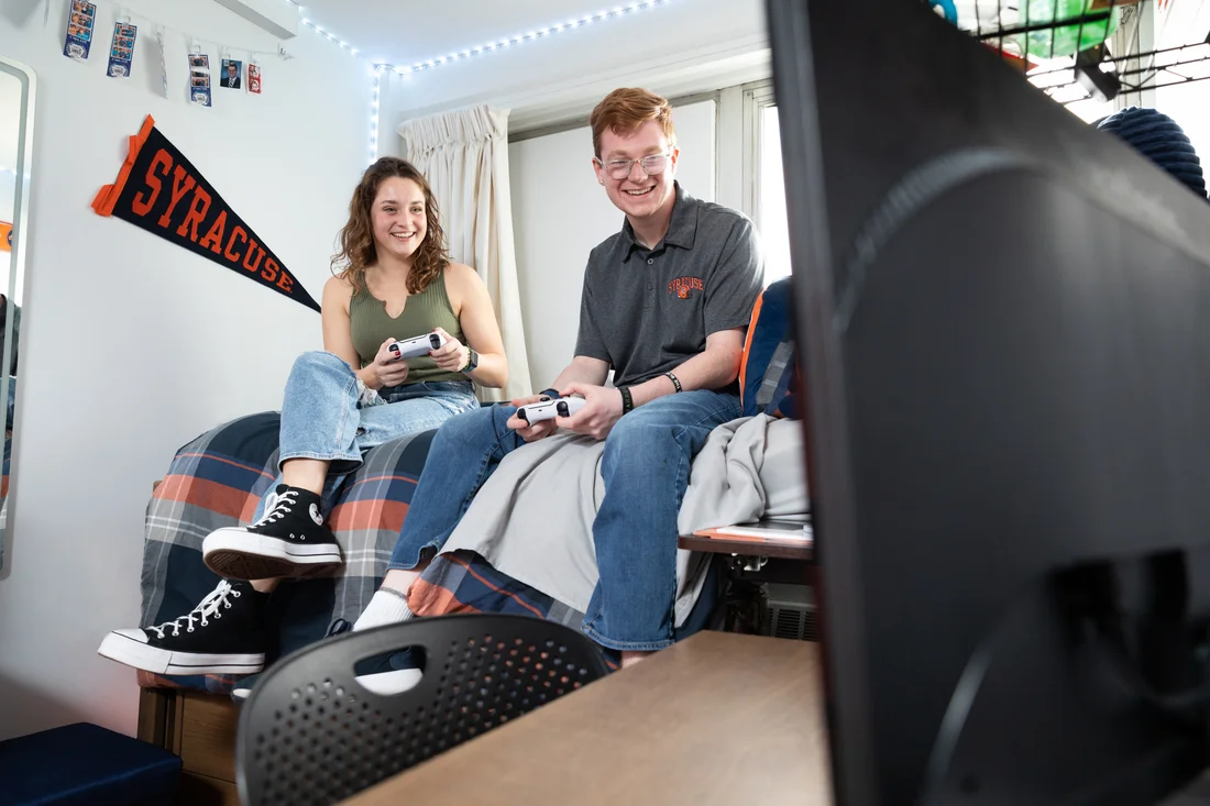 Two students playing a game and talking in dorm room.