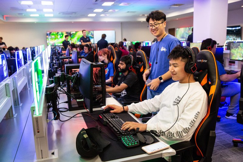 Students in esports room gather around monitor in row of gaming computers